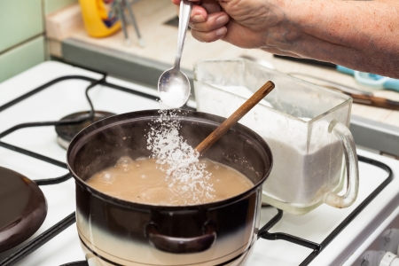 Detail of pouring salt into boiling soup in pot on cooker.の写真素材