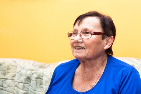 Happy smiling senior woman sitting on sofa over yellow background.の写真素材
