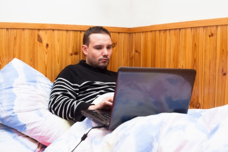 Young man lying in bed and using laptop.の写真素材