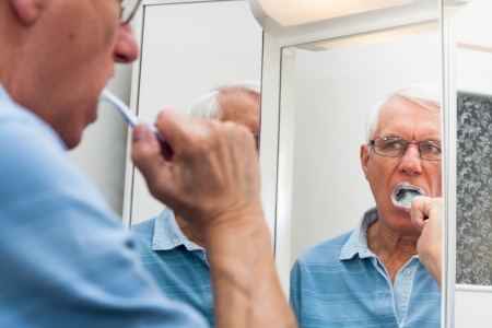 Close up of senior man reflected in mirror brushing his teeth.の写真素材