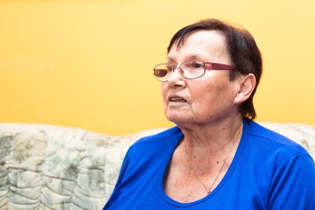 Smiling elderly woman sitting on sofa over yellow background.の写真素材