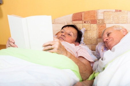Close up of happy senior couple reading book in bed.の写真素材