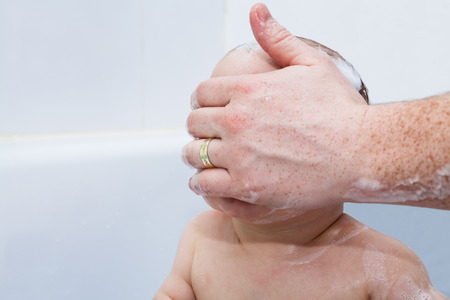 Baby boy in bath and adult male hand covering his face.の写真素材