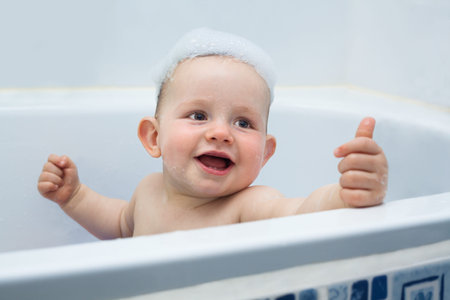 Cute ecstatic baby boy enjoying bath and showing thumb up.