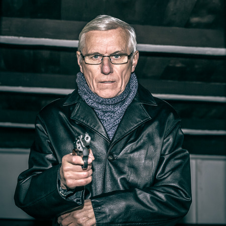 Portrait of dangerous senior man aiming a gun at you.の写真素材