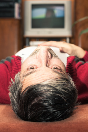 Closeup of senior man lying in front of TV and looking upの写真素材