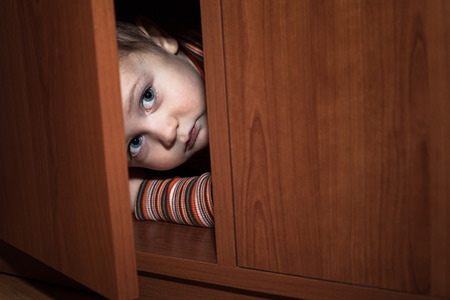 Scared child boy hiding in wardrobeの写真素材