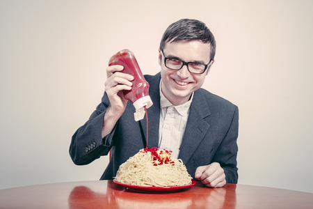 Positive consumerism concept. Happy businessman pouring ketchup on large dish of pasta.の写真素材