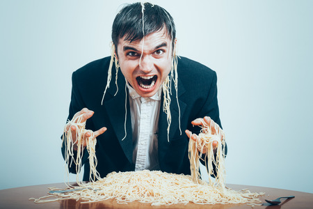 Crazy consumerism concept. Mad nasty businessman eating pasta on the table.の写真素材