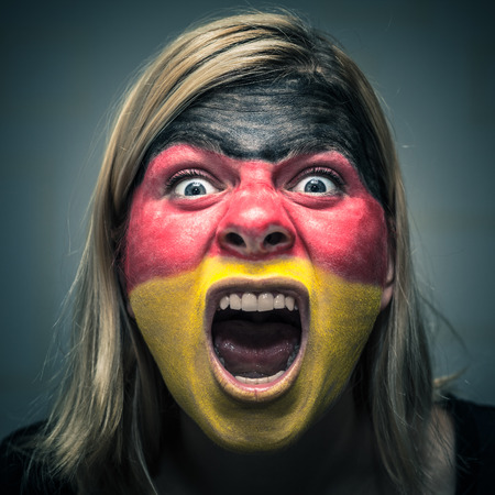 Portrait of angry woman with flag of Germany painted on face.の写真素材