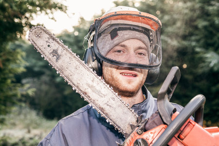 Portrait of professional gardener with chainsaw standing in the garden.