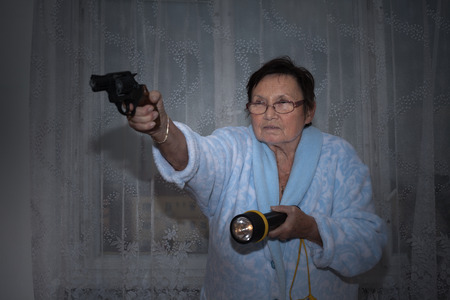 Scared senior woman aiming a gun and torch.の写真素材