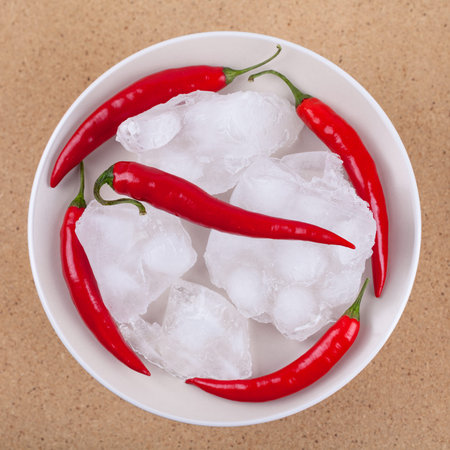 Fresh red hot chili peppers with ice on plate, over wooden background.の写真素材