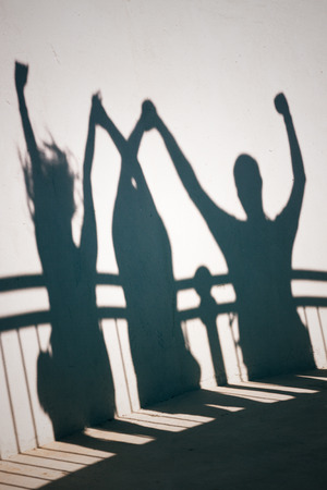 Creative photo of happy people shadows on white wall holding handsの写真素材