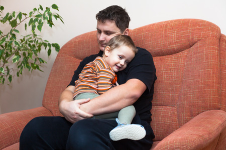 Happy father hugging his child, sitting on sofa at homeの写真素材