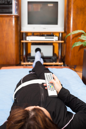 Middle aged woman with remote control watching TV at home. Shallow depth of field with focus on remote control.の写真素材