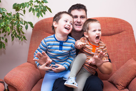Happy children boys and daddy having fun on sofa at homeの写真素材