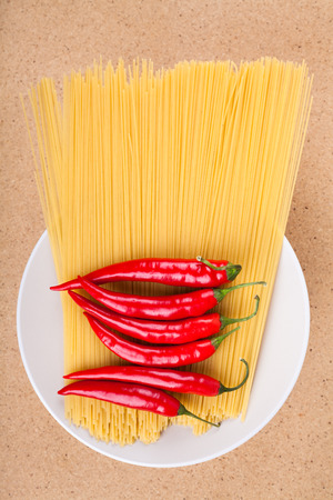 Plate with fresh chili peppers and dried uncooked pasta, over wooden background.の写真素材
