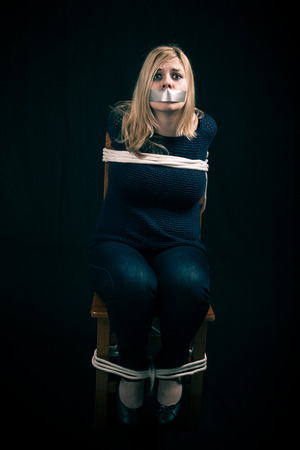 Kidnapped woman hostage with tape over mouth and tied up with ropeの写真素材