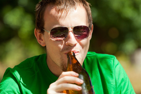 Young happy man drinking beer from bottle outdoors.の写真素材