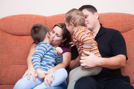 Happy parents kissing with their children at homeの写真素材
