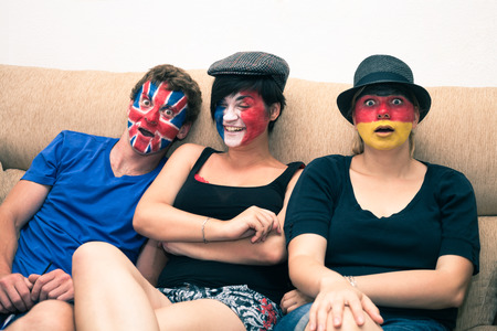 Group of funny people with painted flags on their faces and sitting on sofa.の写真素材