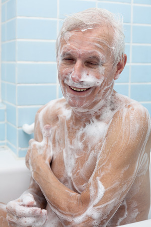 Happy senior man washing his body with soap in bath.の写真素材