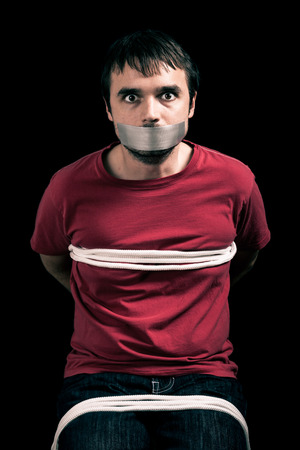 Kidnapped man hostage with tape over mouth and tied up with ropeの写真素材
