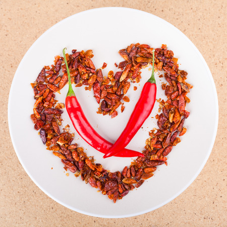 Hot love concept, red chili peppers on plate arranged in heart shape.の写真素材