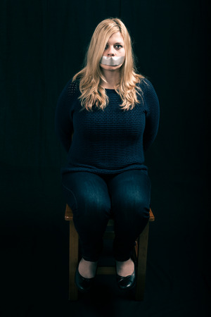 Portrait of scared kidnapped woman hostage with tape over her mouthの写真素材