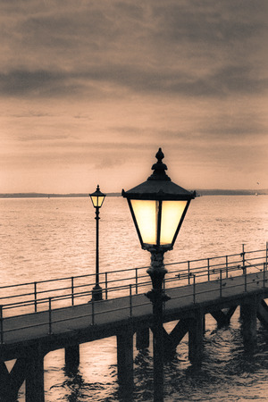 Moody sky and vintage streetlamp on the coast. Toned grainy 35mm film scan.の写真素材