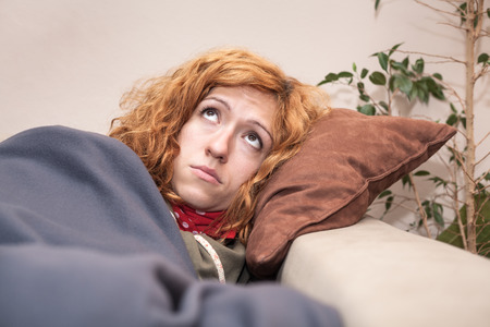 Sad lonely redhead woman looking up and resting on the sofa at home.の写真素材