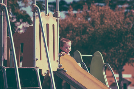 Vintage looking photo of a child boy on a slide at children playground.の写真素材