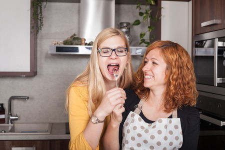 Excited girlfriends enjoying food and feeding each other in the kitchen at home.の写真素材