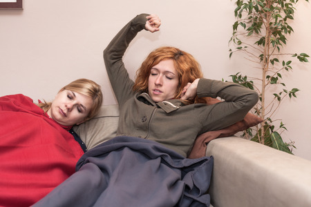 Tired girlfriends stretching and sleeping together on the sofa at home.の写真素材
