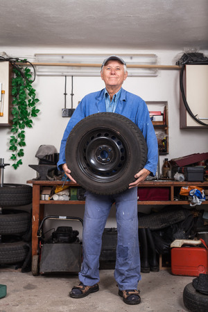 Portrait of happy senior worker changing tire in the garage.の写真素材