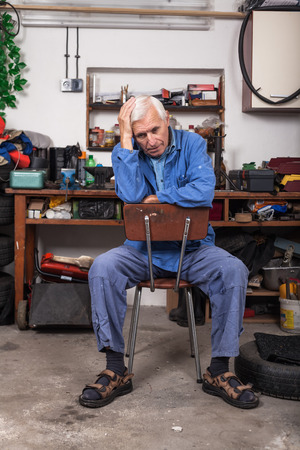 Portrait of frustrated senior worker sitting on the chair in his workshop.の写真素材