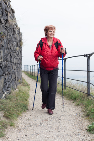 Active senior woman Nordic walking on rocky trail outdoors.の写真素材
