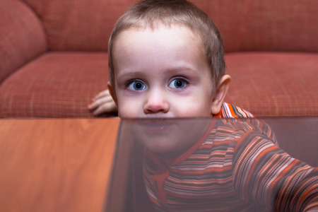 Cute child boy hiding behind tableの写真素材
