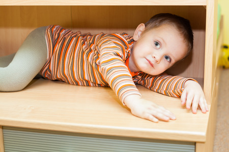 Cute child boy hiding in cupboard at homeの写真素材