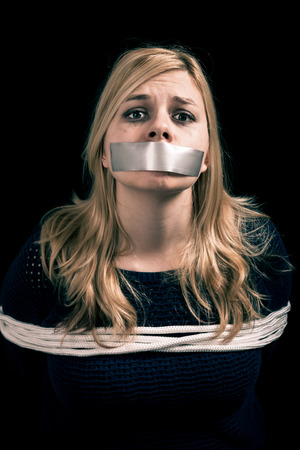 Kidnapped woman hostage with tape over mouth and tied up with ropeの写真素材