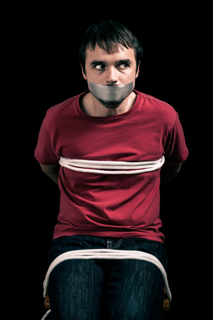 Kidnapped man hostage with tape over mouth and tied up with ropeの写真素材