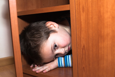 Scared child boy hiding in wardrobeの写真素材