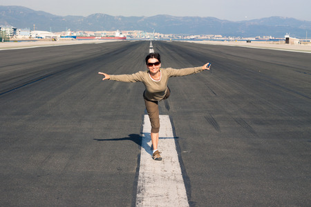 Happy woman tourist imitating airplane at the airport runway.の写真素材