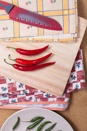 Fresh red hot chili peppers with knife on chopping board.の写真素材