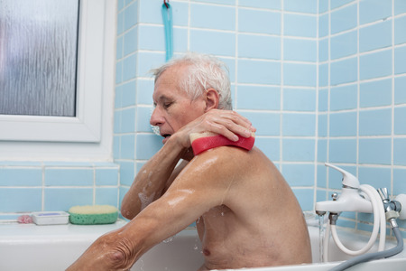 Senior man washing his body with soap sponge in bath.の写真素材