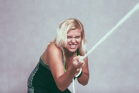 Excited strong sporty woman pulling the rope. Determination, effort and female power concept.の写真素材