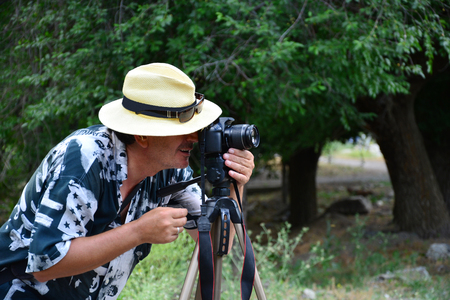 Male hipster tourist dressed in trendy clothing taking picture on his professional vintage camera while sitting in urban coffee shop near the window.Male photographer making photos for his travel blogの写真素材