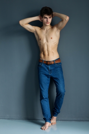 sexy man with naked torso in jeans posing near grey wall, daylightの写真素材