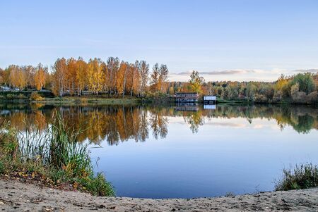 The Boat Shed on quiet colorful lake that reflects autumn leaves, blue sky with cloudsの写真素材